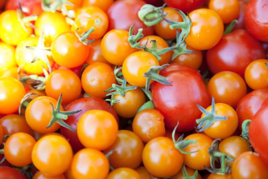 A close-up view of a pile of orange and red cherry tomatoes with stems, some highlighted by sunlight, reminiscent of the vibrant colors found in Sonoma’s finest Pinot Noir and Chardonnay vineyards.